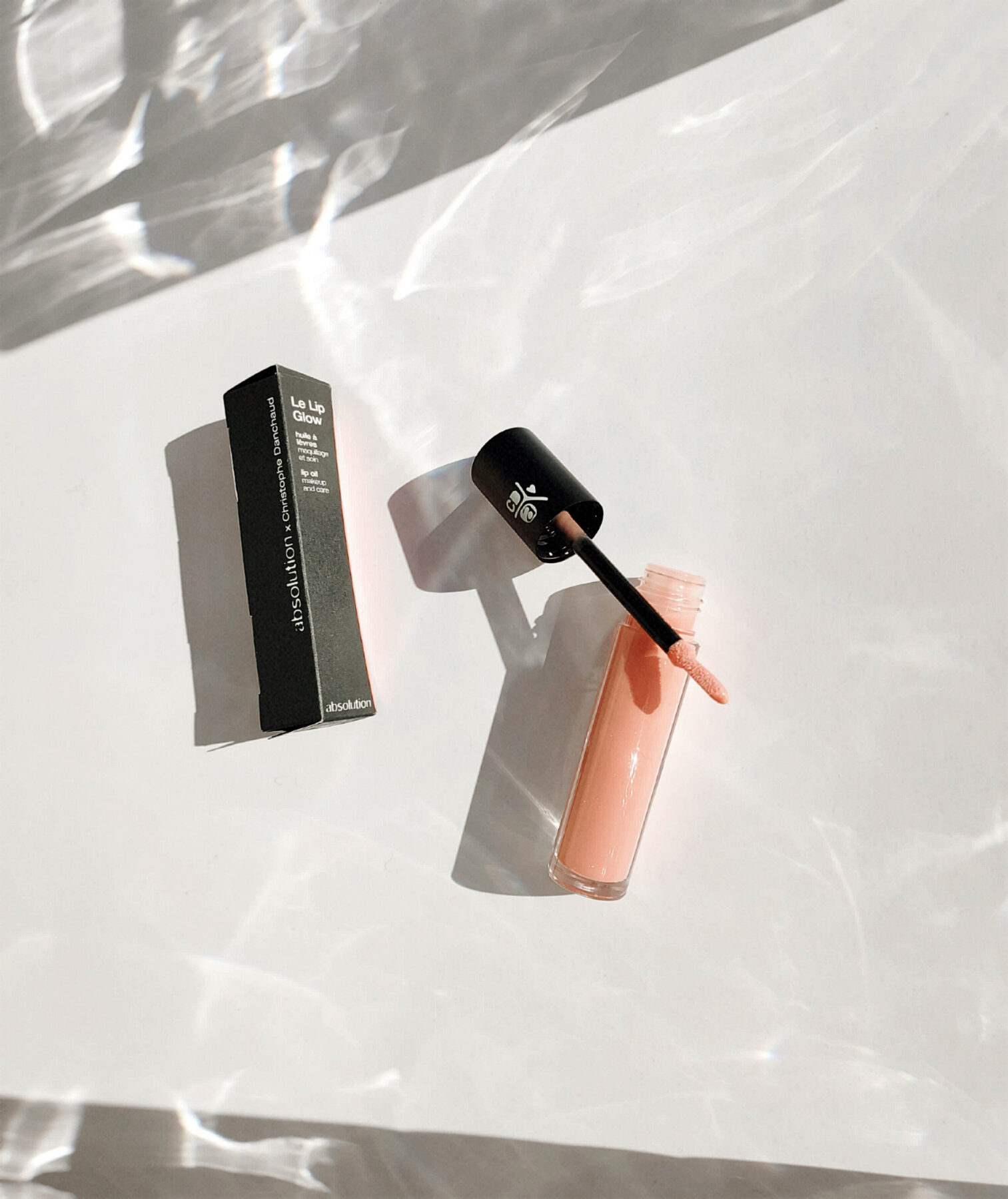 Serum en lipgloss in zonlicht op een lichte ondergrond